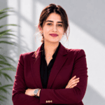 Confident professional woman in a burgundy blazer posing with arms crossed in a modern office