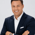 Professional businessman in a navy suit smiling with arms crossed against a white background
