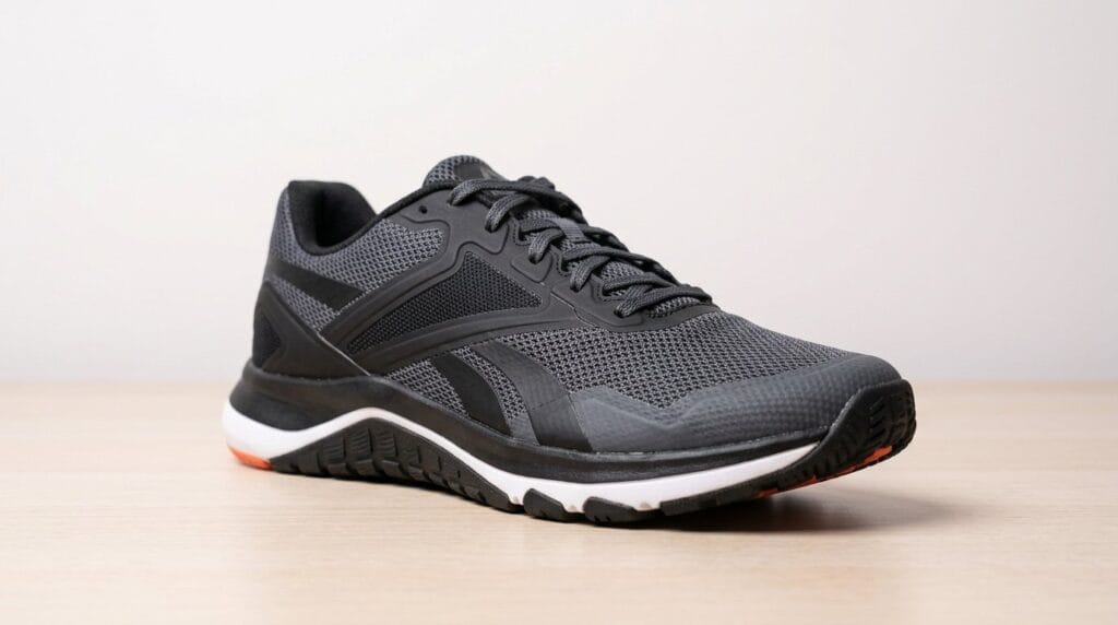 Black athletic cross-training shoe with white and orange sole on a wooden surface, lit by soft directional light