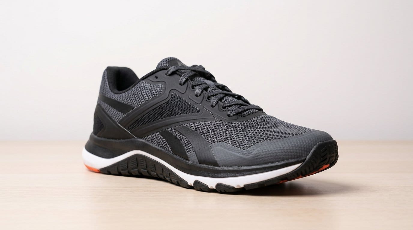 Black athletic cross-training shoe with white and orange sole on a wooden surface, lit by soft directional light