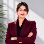 Confident professional woman in a burgundy blazer posing with arms crossed in a modern office